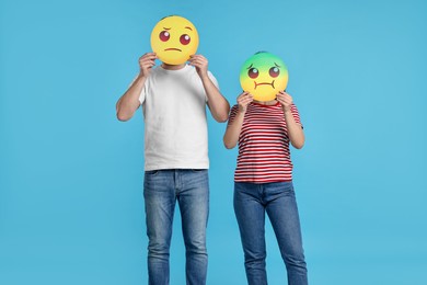 People covering faces with emoticons on light blue background