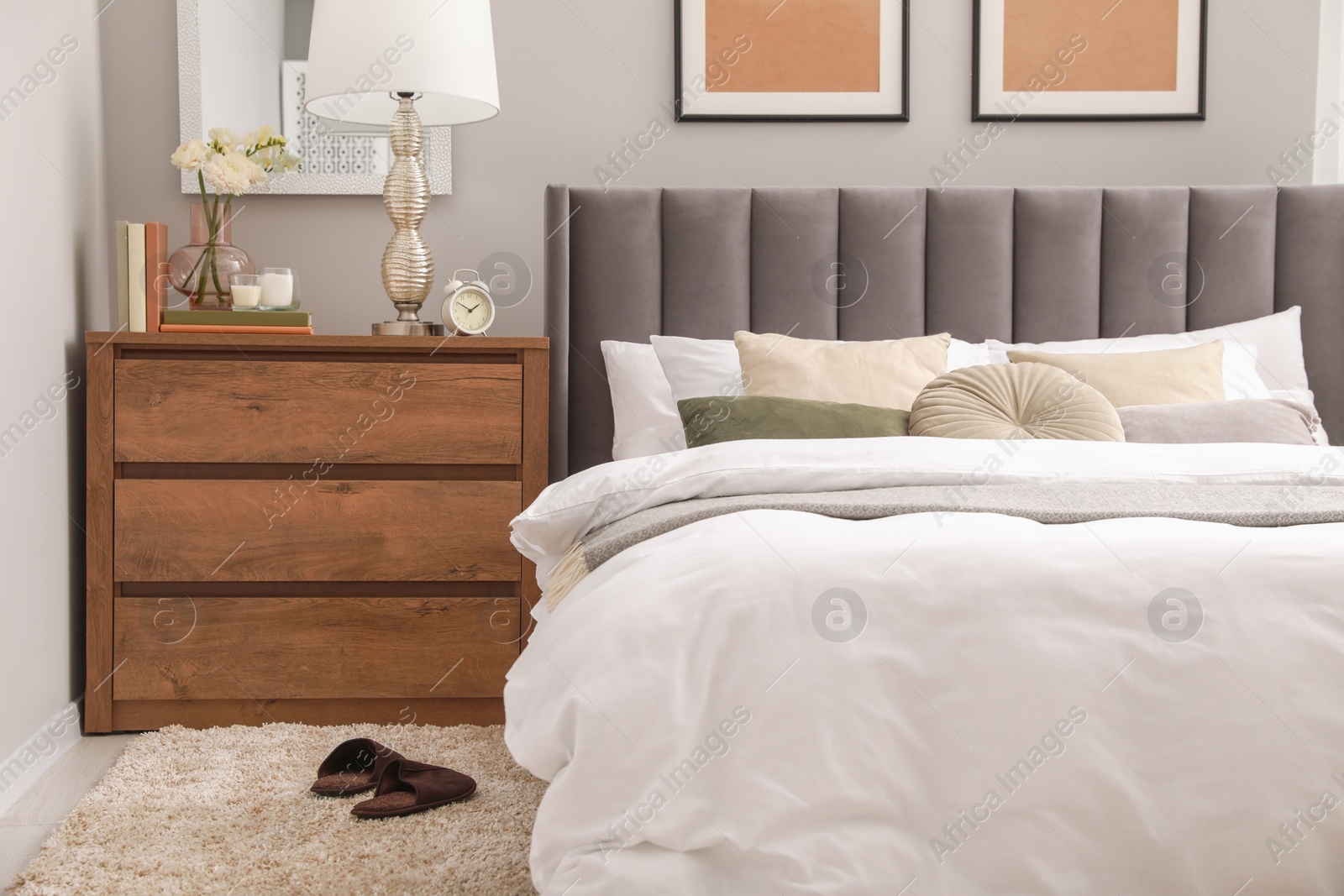 Photo of Comfortable bed with cushions, lamp and different decor on wooden chest of drawers in room. Stylish interior