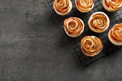 Photo of Cooling rack with freshly baked apple roses on grey table, top view. Space for text