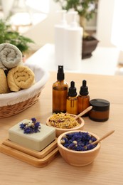 Soap bar, dry flowers, bottles of essential oils, jar with cream and towels on wooden table indoors. Spa time