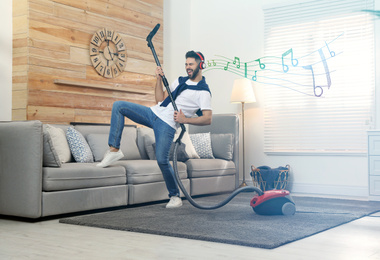 Young man listening to music through headphones while vacuuming at home