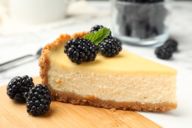 Piece of delicious cheesecake decorated with blackberries on table