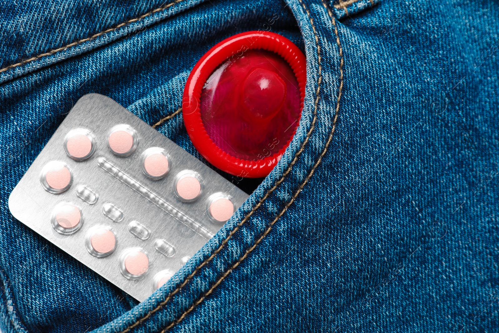 Photo of Closeup view of jeans with red condom and birth control pills in pocket. Safe sex concept