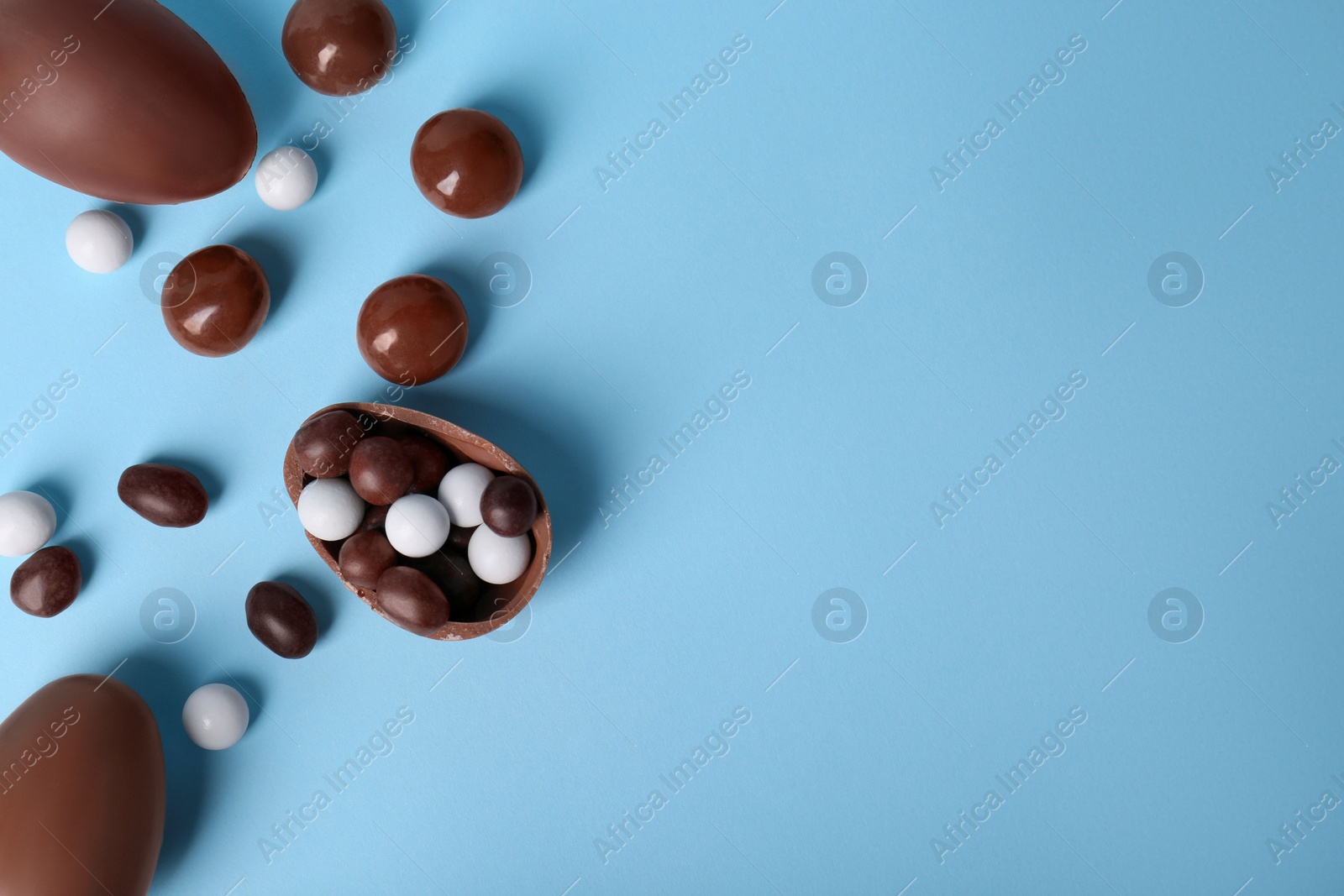 Photo of Tasty chocolate eggs and different sweets on light blue background, flat lay with space for text