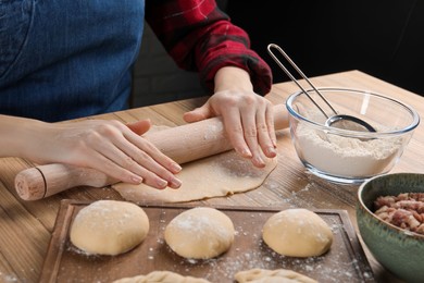Photo of Woman rolling dough for chebureki at wooden table, closeup