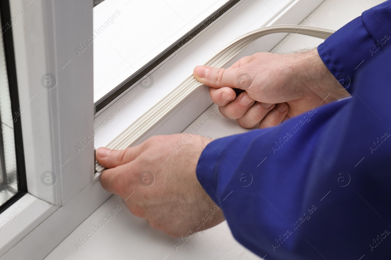 Photo of Worker putting rubber draught strip onto window indoors, closeup