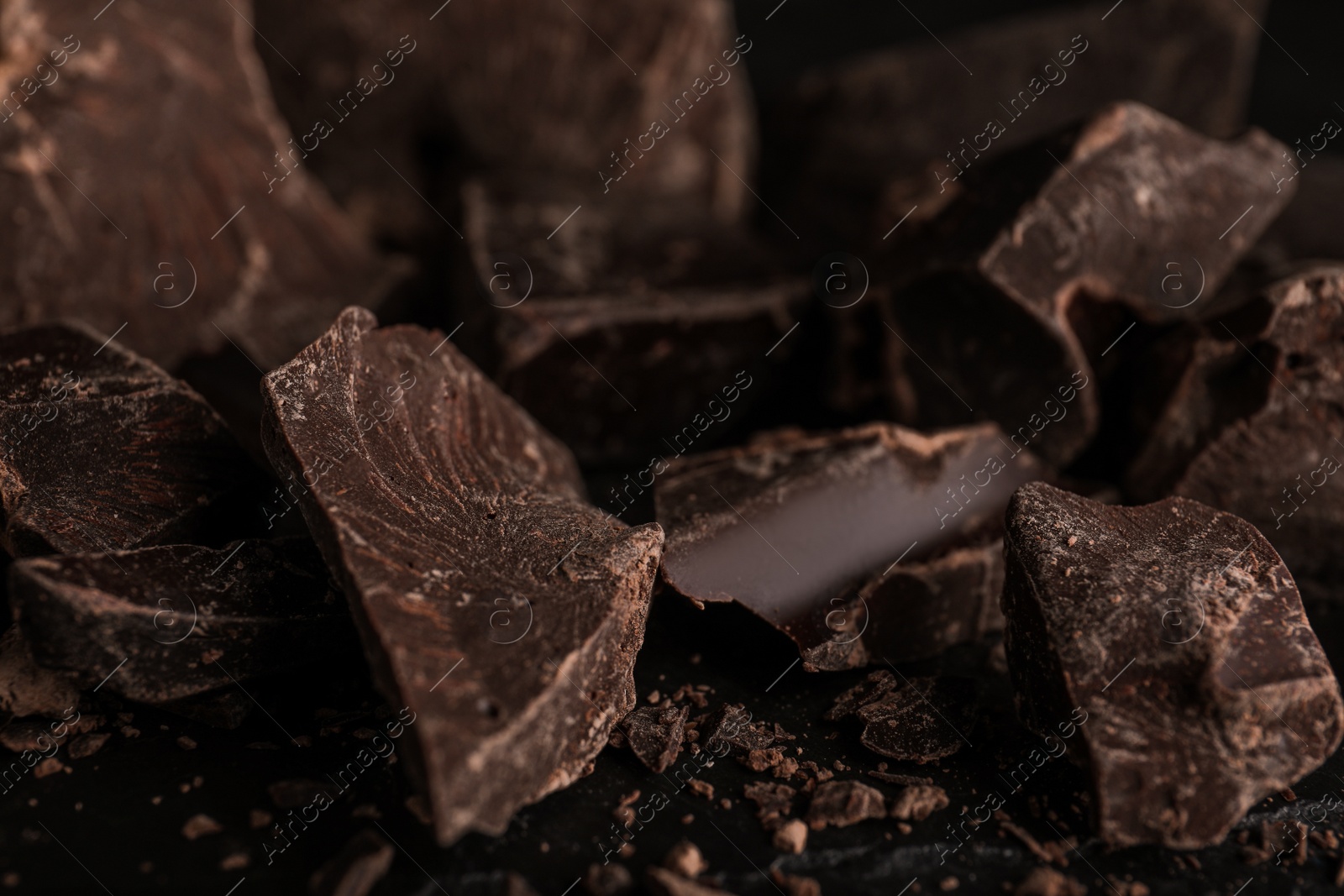 Photo of Pieces of dark chocolate on black table, closeup