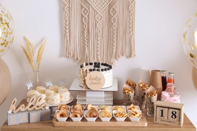 Photo of Baby shower party. Different delicious treats on wooden table and decor near light wall