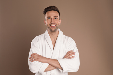 Photo of Happy young man in bathrobe on brown background