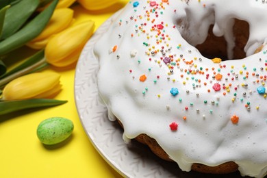 Photo of Easter cake with sprinkles and tulips on yellow background, closeup