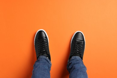 Man in stylish sneakers standing on orange background, top view