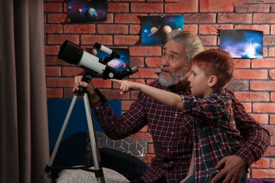Little boy with his grandfather using telescope to look at stars in room