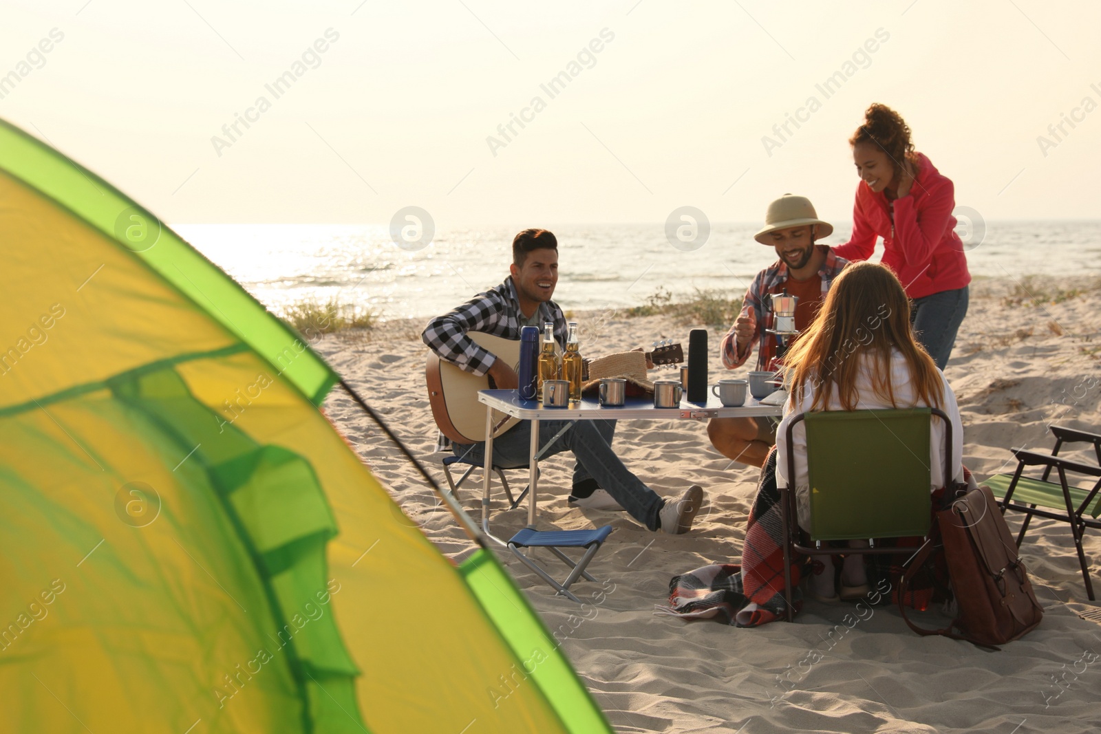 Photo of Friends resting near camping tent on sandy beach