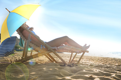 Image of Young couple relaxing in deck chairs under umbrella for sun protection on beach near sea