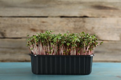 Photo of Fresh radish microgreens in plastic container on turquoise wooden table