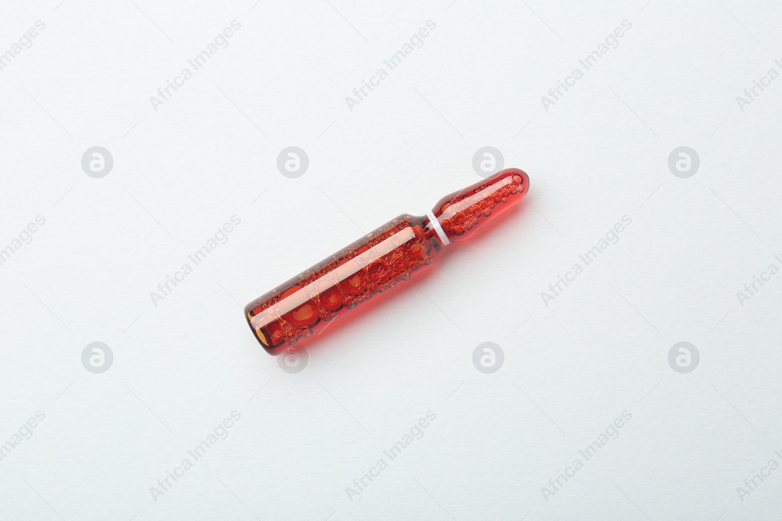 Photo of Glass ampoule with liquid on white background, top view