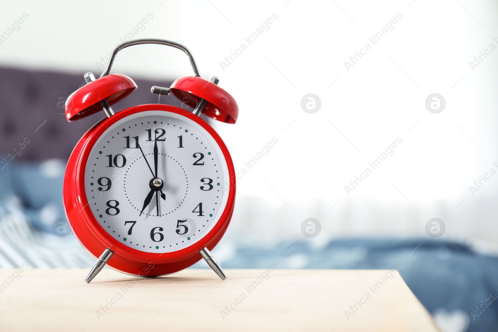 Photo of Analog alarm clock on table in bedroom. Time of day