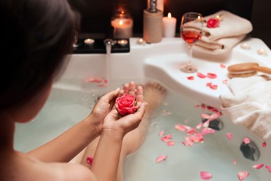 Photo of Woman holding rose flower while taking bath, closeup. Romantic atmosphere