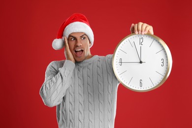 Photo of Man in Santa hat with clock on red background. New Year countdown