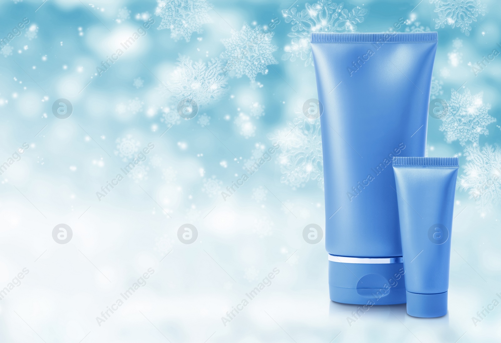 Image of Tubes of cosmetic product on light blue background with blurred snowflakes, space for text. Winter skin care