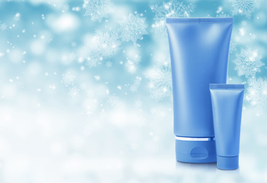 Image of Tubes of cosmetic product on light blue background with blurred snowflakes, space for text. Winter skin care