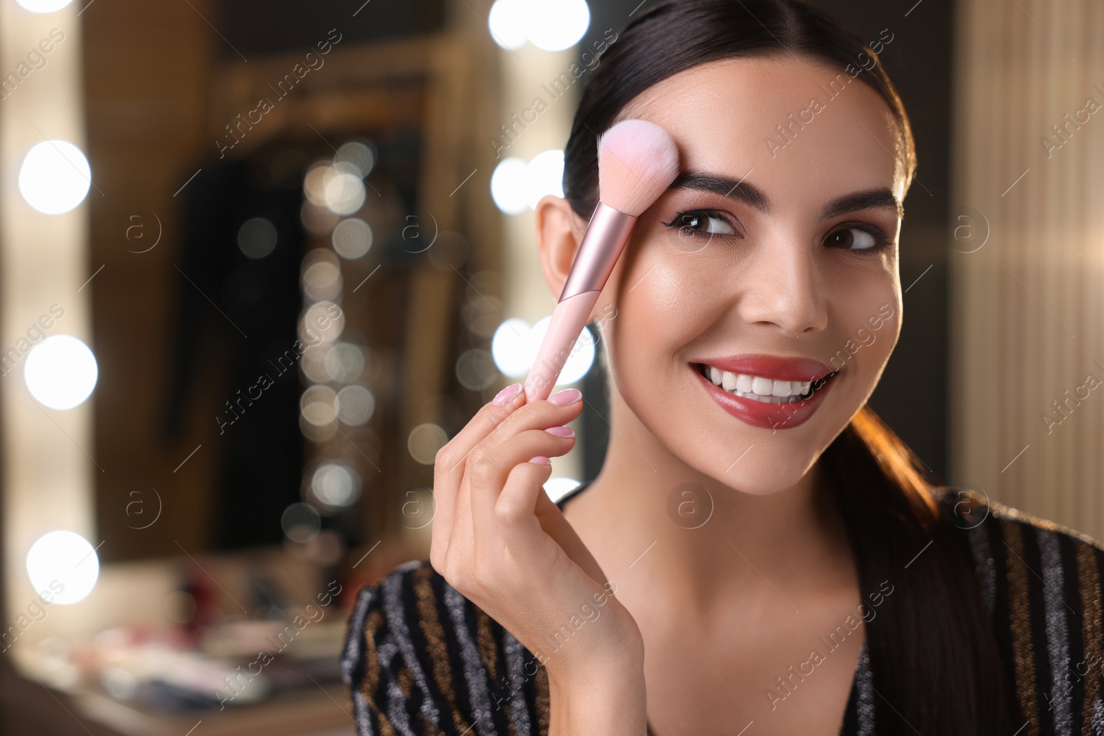 Photo of Bright makeup. Beautiful woman applying face powder in dressing room. Space for text