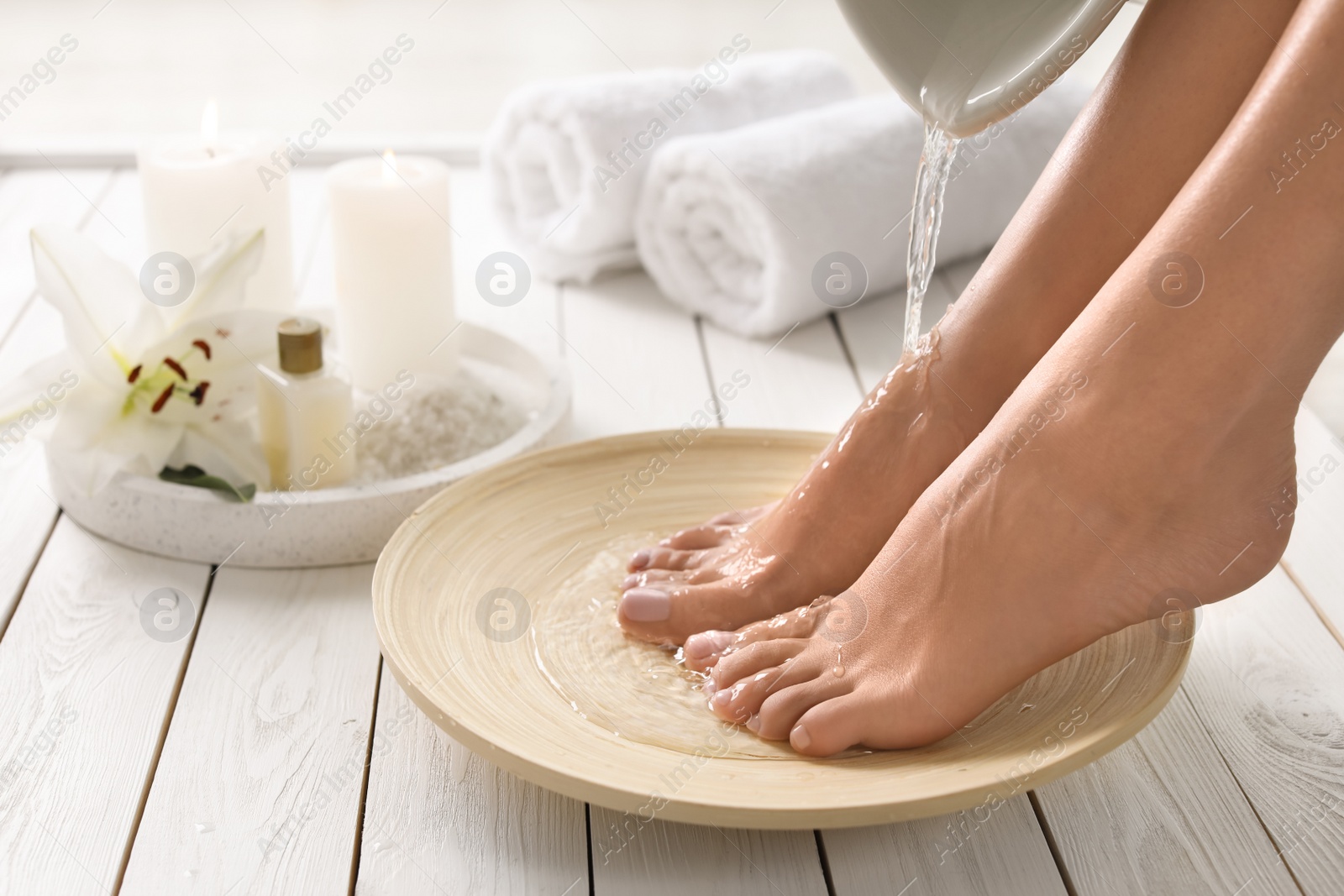 Photo of Closeup view of woman filling dish with water for foot bath indoors. Spa treatment