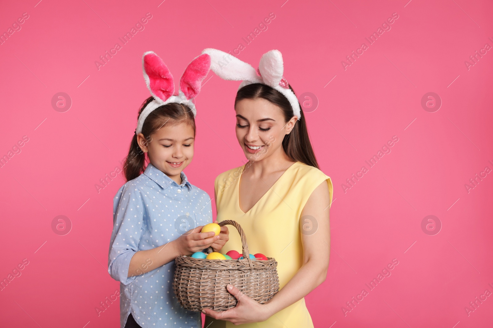 Photo of Mother and daughter in bunny ears headbands with Easter eggs on color background