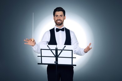 Photo of Happy professional conductor with baton and note stand on grey background
