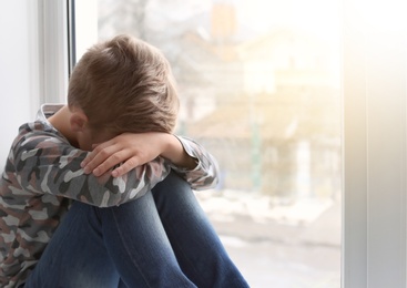 Photo of Lonely little boy near window indoors. Child autism