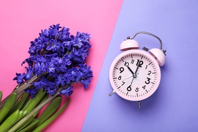 Pink alarm clock and beautiful hyacinth flowers on color background, flat lay. Spring time