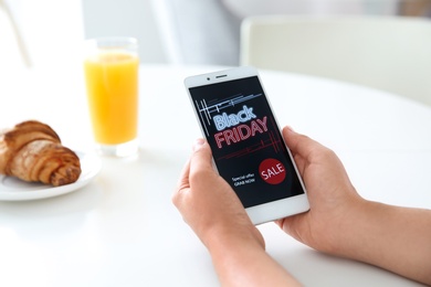 Woman shopping online using smartphone at table indoors, closeup. Black Friday Sale