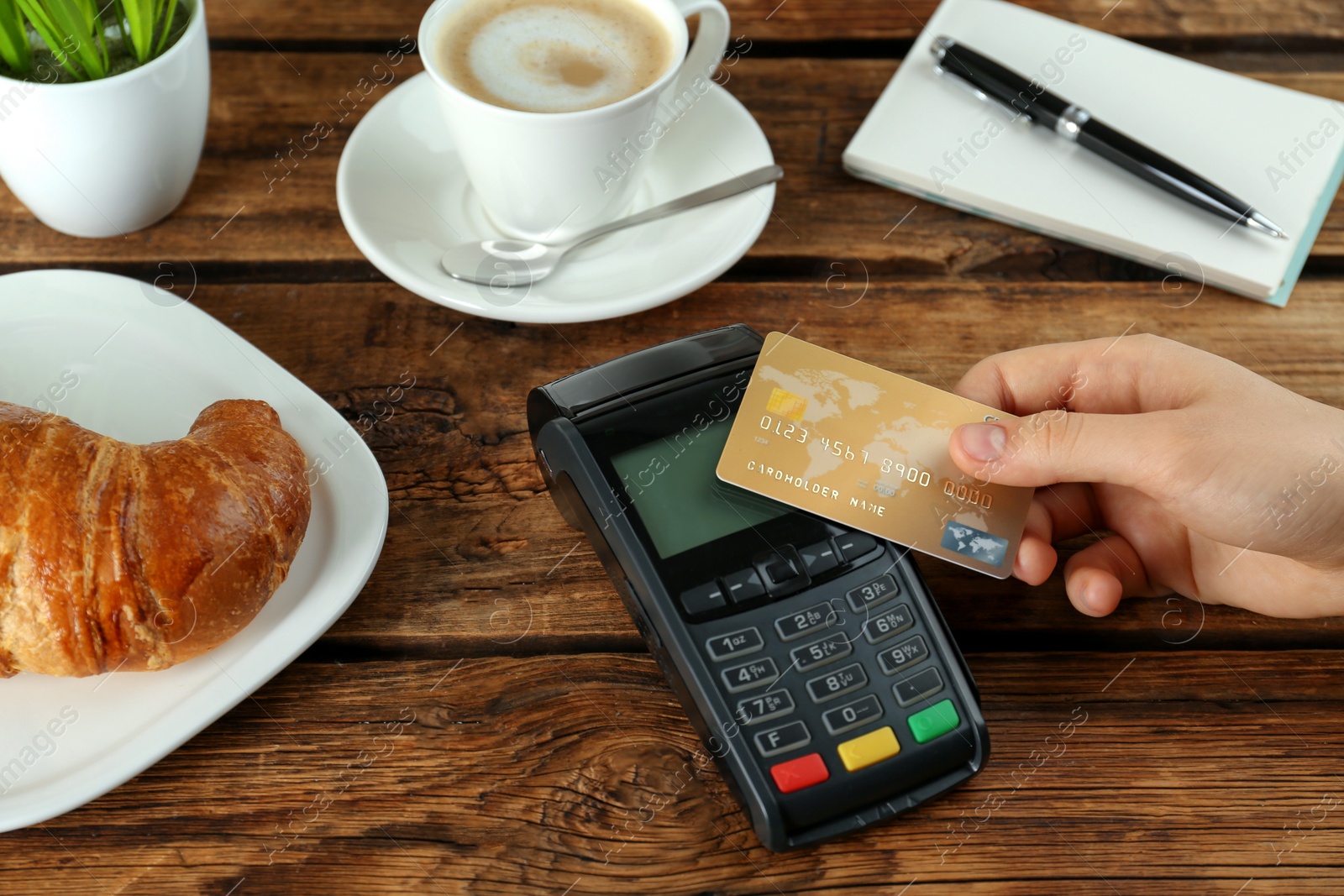 Photo of Woman with credit card using modern payment terminal at wooden table, closeup