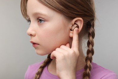 Photo of Little girl with hearing aid on grey background, closeup