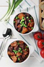 Photo of Delicious beef stew with carrots, peas and potatoes served on white wooden table, flat lay