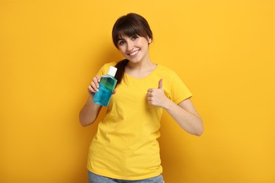 Photo of Young woman with mouthwash showing thumbs up on yellow background