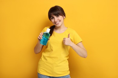 Young woman with mouthwash showing thumbs up on yellow background