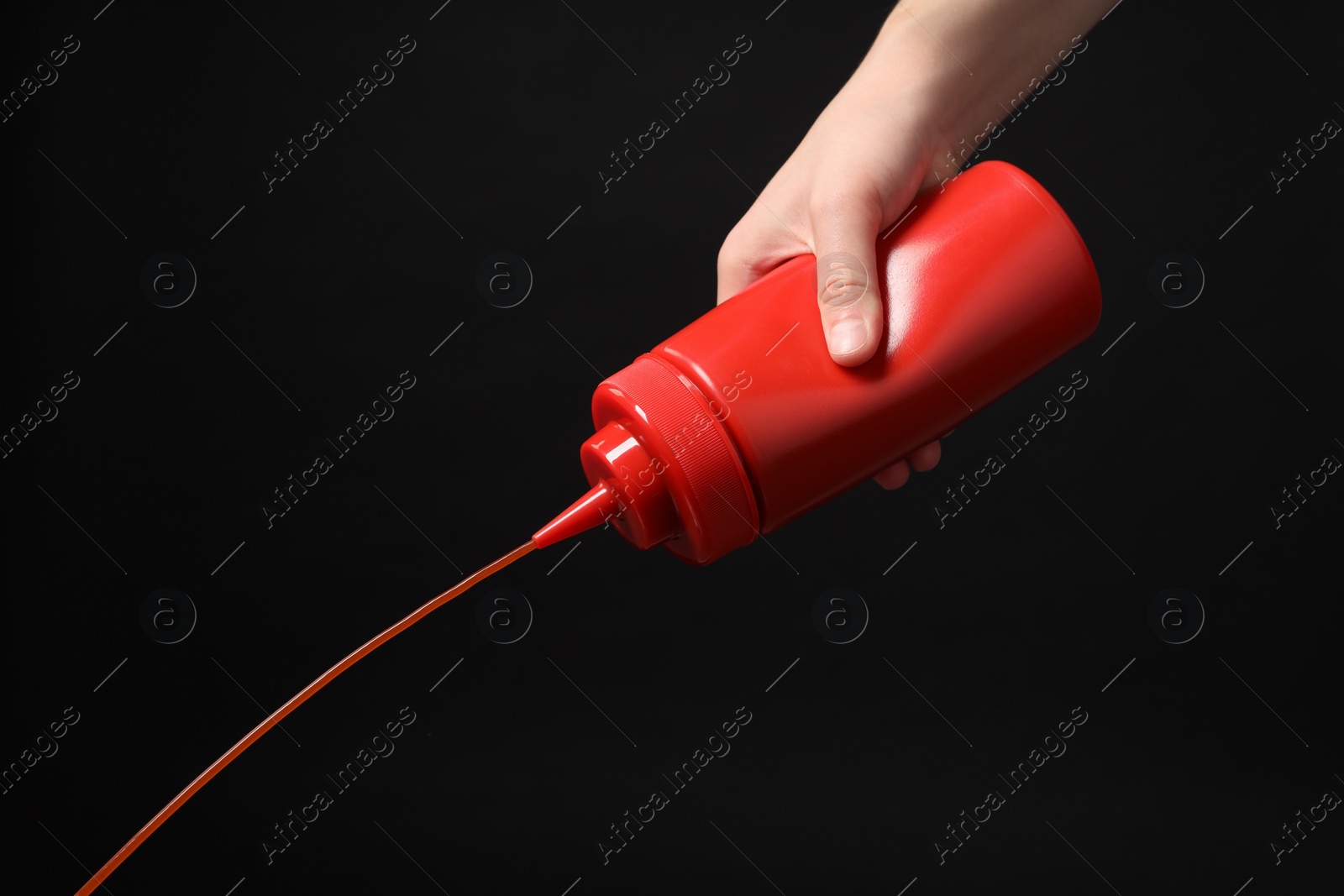 Photo of Woman pouring tasty ketchup from bottle on black background, closeup