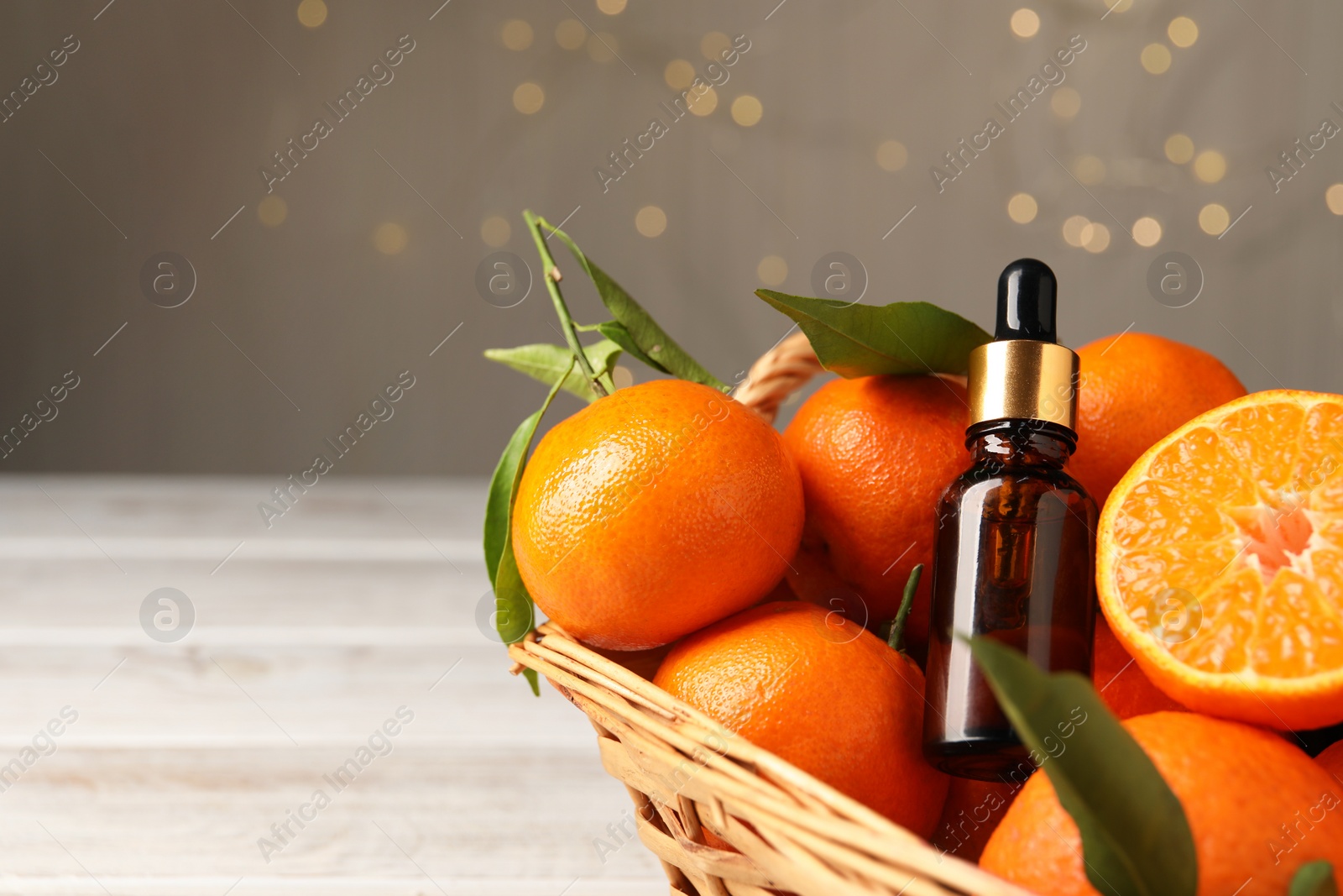 Photo of Bottle of tangerine essential oil and fresh fruits in basket. Space for text