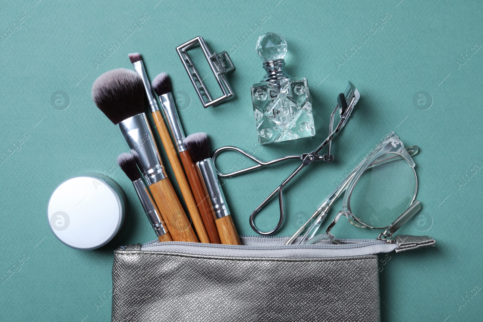 Photo of Cosmetic bag with makeup products and beauty accessories on blue-gray background, flat lay