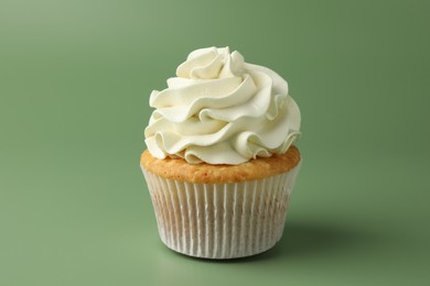 Photo of Tasty vanilla cupcake with cream on green background, closeup