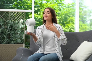 Photo of Woman enjoying air flow from portable fan at home. Summer heat