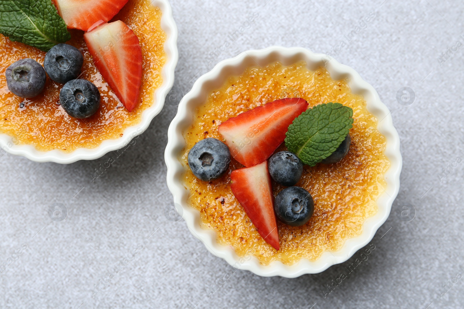 Photo of Delicious creme brulee with berries and mint in bowls on grey textured table, top view