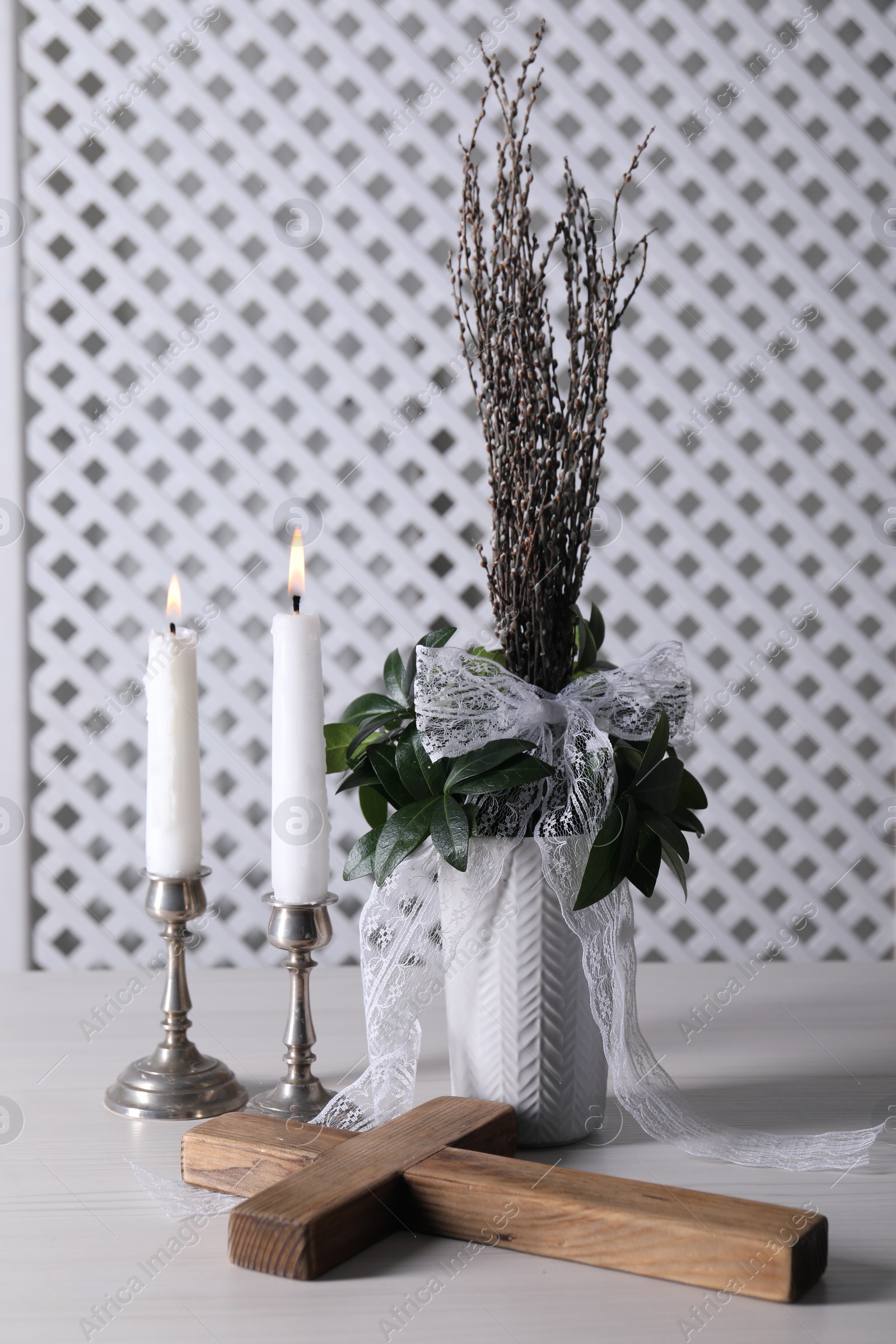 Photo of Burning candles, bouquet with willow branches and cross on white wooden table