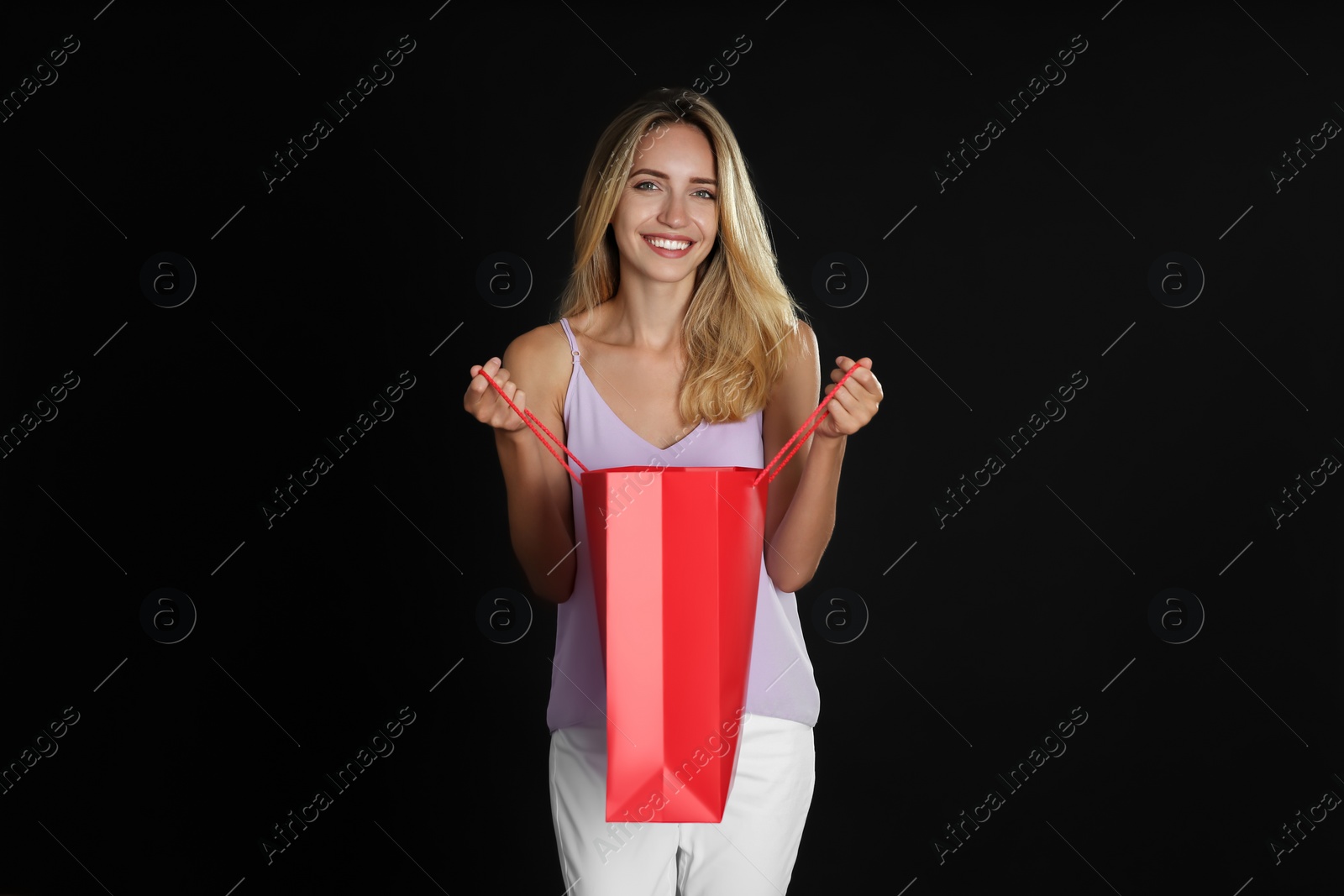 Photo of Happy young woman with shopping bag on dark background. Black Friday Sale