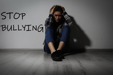 Image of Message STOP BULLYING and abused teen girl crying near white wall