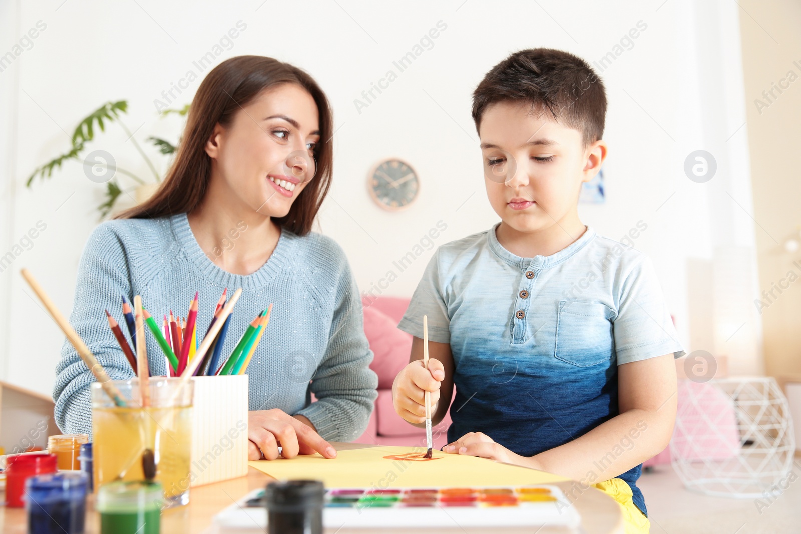 Photo of Cute little child painting at table with young mother in playing room