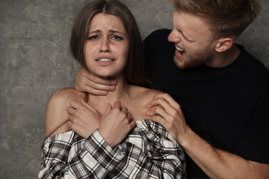 Photo of Man choking young woman on grey background. Stop sexual assault