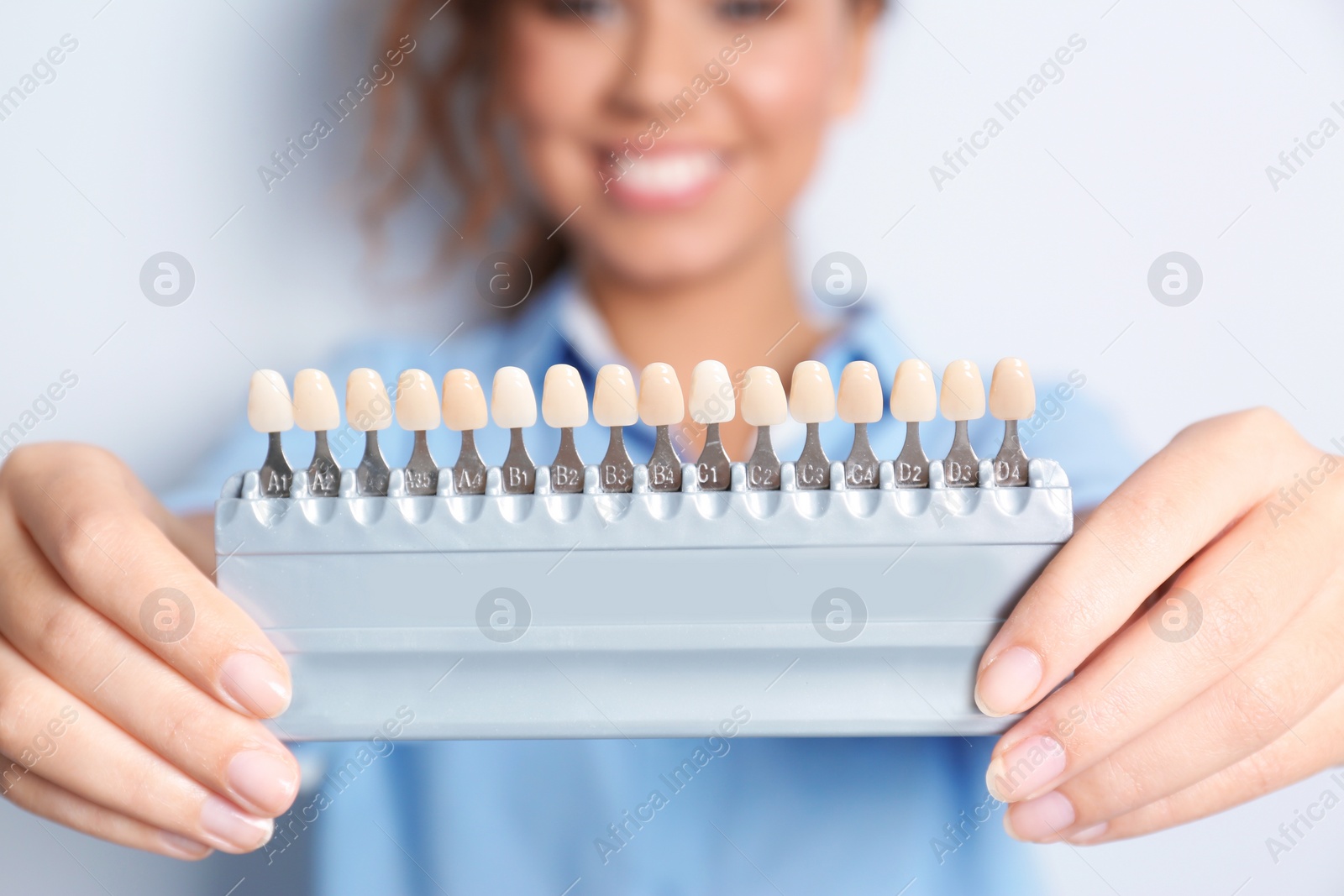 Photo of Young African-American woman with teeth color samples against light background, focus on palette