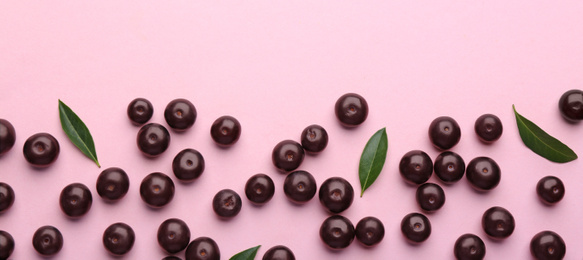 Fresh acai berries and green leaves on pink background, flat lay. Space for text